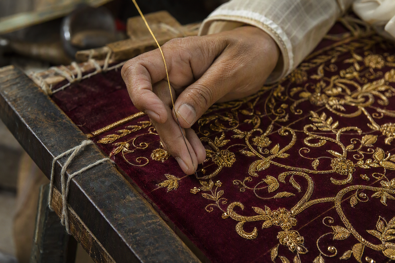 Artisan hand-embroidering gold zardozi on burgundy fabric
